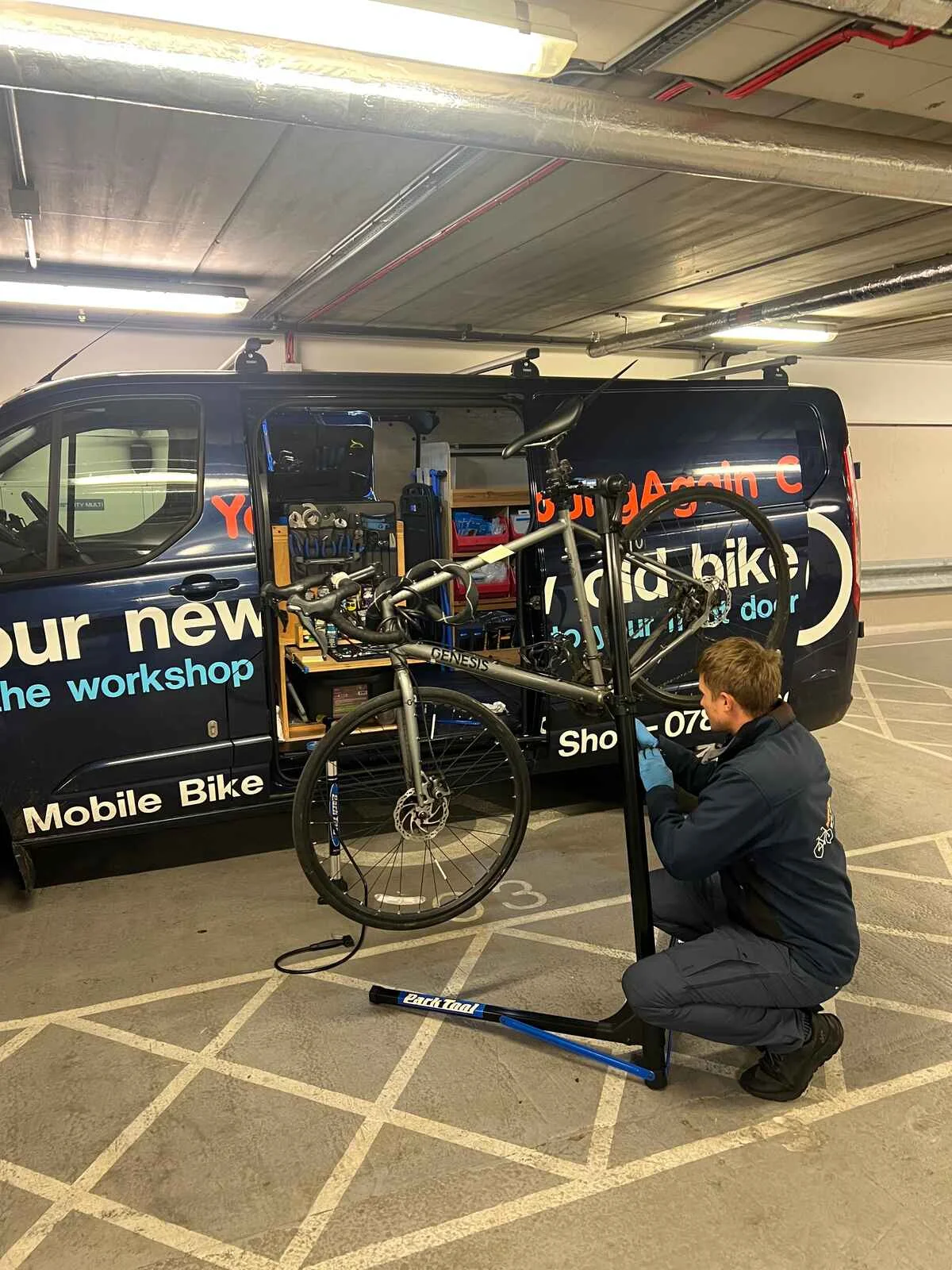 A YoungAgain Cycles mechanic servicing a bike on a portable stand beside the mobile workshop van